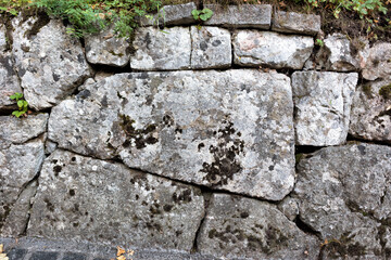 Texture wall made of big grey stones covered with moss and grass.