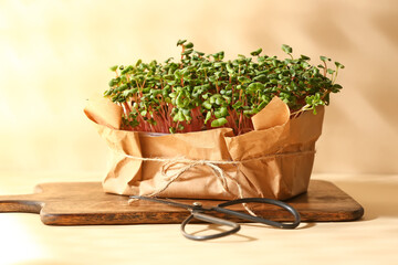 Wooden board with fresh micro green and scissors on color background