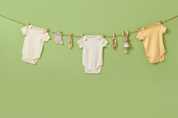 Different baby clothes and toys hanging on rope against color background