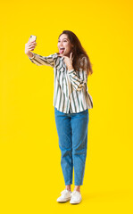 Beautiful young woman taking selfie on yellow background