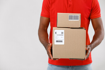 African-American delivery man with parcels on grey background