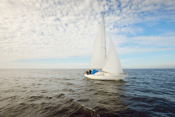 White sloop rigged yacht sailing in an open sea. Clear sky, cloudscape. A view from the sailboat....