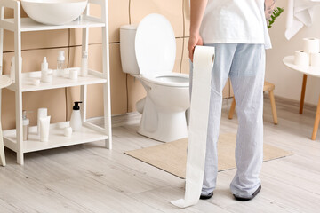 Young man with toilet paper in bathroom