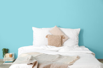 Comfortable bed with soft linens, organizer and paper cup of coffee near blue wall