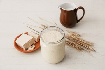 Glass jar with fresh sourdough on white wooden background