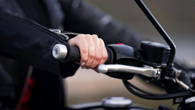 Female motorcyclist hand twists accelerometer lever while standing at city. Culture and aesthetics of vintage cafe racers, classic motorbike.
