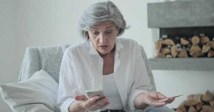 Online banking risks, fraud, and the card limiting idea. Senior old elderly woman using credit card and mobile phone spending all money on shopping and online gaming. The concept of addiction and debt