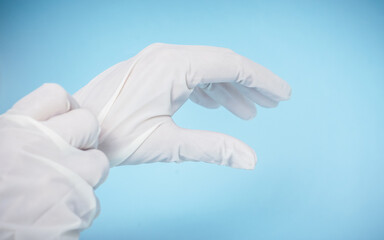 Person putting on surgical gloves. Isolated blue light background. Copy space.