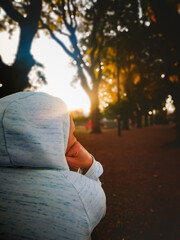 Adult woman photographed from behind wearing a hoodie sitting on a bench during an autumn sunset.