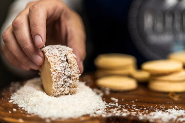 Hand of an unrecognizable person making homemade argentine alfajor spreading it grated coconut