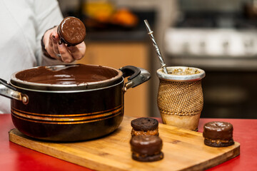 Hand of an unrecognizable person making homemade argentine alfajor dipping it in chocolate sauce