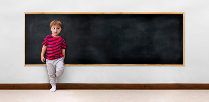 Little boy leaning against a blank blackboard, ready to be written, drawn or used as a mockup.