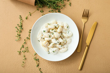 Plate of delicious gnocchi with creamy sauce on beige background