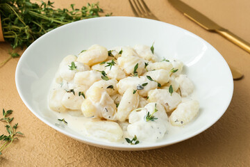 Plate of delicious gnocchi with creamy sauce on beige background