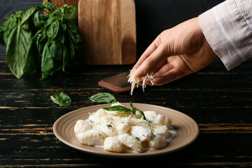 Woman adding Parmesan cheese into plate with delicious gnocchi at table