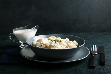 Bowl of tasty gnocchi with creamy sauce on black background