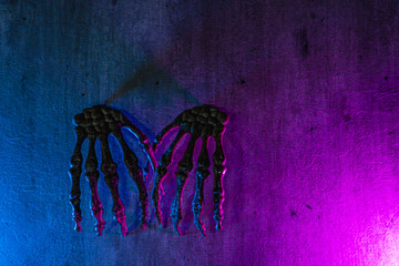 Pair of scary skull hands on texture background with blue and pink colored lights for halloween.