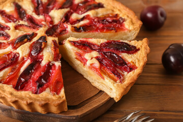 Board with piece of tasty plum pie on wooden background, closeup