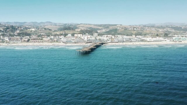 Cinematic ocean pier in Pismo Beach in sunny Southern California, USA. Perfect summer background with copy and text space on blue green ocean, white sandy beach background 4K