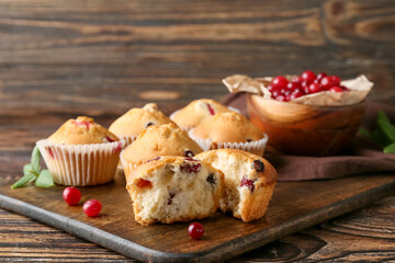 Board with tasty cranberry muffins on wooden background