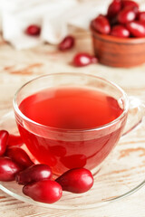 Glass cup of tasty dogwood drink on light wooden background, closeup
