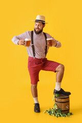 Handsome man in traditional  German clothes and with beer on color background