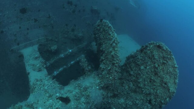 Underwater visual revealing the rusted propeller of a recently scuttled naval shipwreck deep below the ocean.