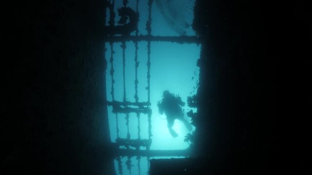 Unique view looking up at a silhouette of a scuba diver passing over a sunken shipwreck.