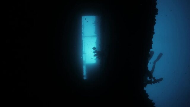 Unique view looking up at a silhouette of a scuba diver passing over a sunken shipwreck.