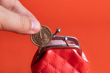 Male hand with 1 American dollar coin and miniature red leather wallet on red background