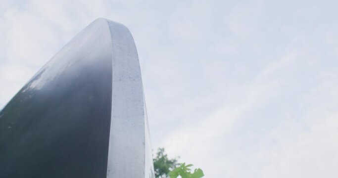 Close up shot of a metal art installation in the great park of Ulm. Camera slides slowly to the right. Sky and clouds reflecting in the installation.