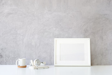 Empty picture frame, headphone, coffee cup and books on white table with loft wall.