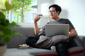 Young man holding credit card and making banking online or shopping online on laptop computer.