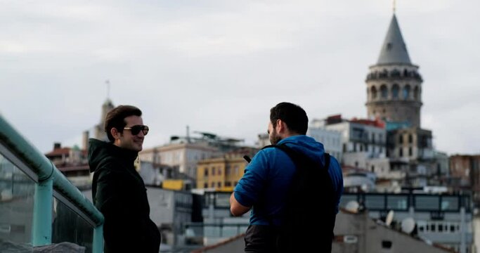 Backstage of studio photoshoot: handsome guy model is posing for a male photographer on the terrace in front of Galata Tower.  People and advertising concept.