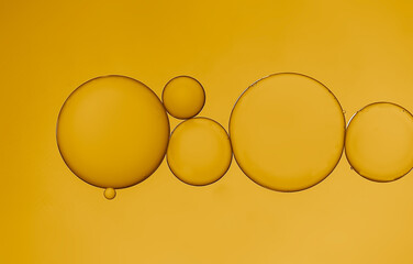 Closeup of water and oil droplets on light golden-yellow background.