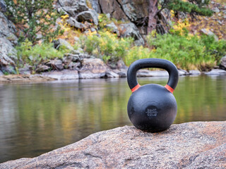 Naklejka na ściany i meble heavy iron competition kettlebell for weight training on a shore of mountain river, outdoor fitness concept