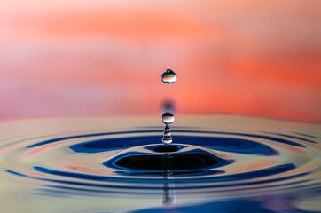 Fototapeta na wymiar Water droplet splash and make perfect ripples on water surface with orange background.