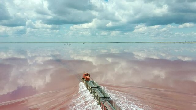 An old train travels on a railway laid in the water across a salt lake. Aerial view. Extraction of salt in Lake Bursol. Russia. 