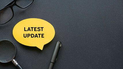 Top view of glasses, pen, magnifying glasses and yellow speech bubble written with Latest Update on...