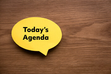 Top view of yellow speech bubble written with Today's Agenda on wooden background with copy space.