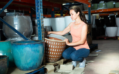 Fototapeta na wymiar Positive woman customer holding big decorative clay vase in the shop