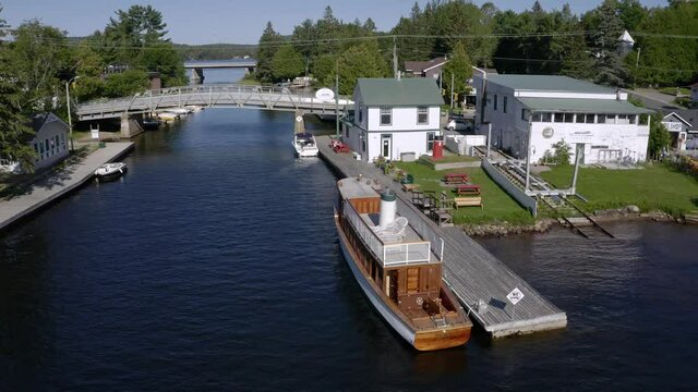 Drone shot of small town of Dorset Ontario with bridges over the river, boats docked and an old wooden ship