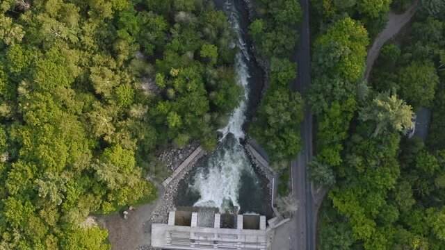 Overhead drone shot following a dammed river with whitewater rapids beside a road with car driving