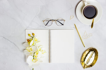 Notebook with coffee, golden pen and orchid over the white marble table. 