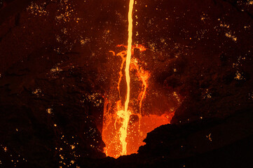 Liquid cast iron is poured into the ladle in a thin stream. Lots of sparks.