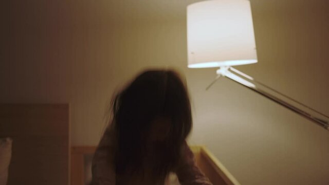 A three-year-old girl in her crib does not want to sleep, jumps energetically, plays. Children's room at dusk: a hyperactive child dances before bed. Night light in the background