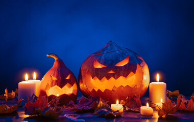 Two autumn pumpkin lanterns with horrible carved faces for Halloween in candle lighting on a blue...