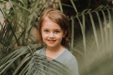 The face of a little girl surrounded by tropical leaves. A closeup portrait of a beautiful baby with perfect skin and blonde hair. Natural cosmetics, health, cleanliness, skin care, beauty concept