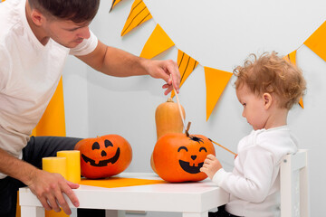 Fototapeta premium Halloween family activity, pumpkin painting process. Cute child drawing scary face. Holiday preparation, party decor