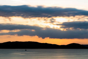 Naklejka premium Stunning sunrise over the silhouette of a coastline bathed by a calm sea. Cloudy, dramatic sky, Sardinia, Italy.